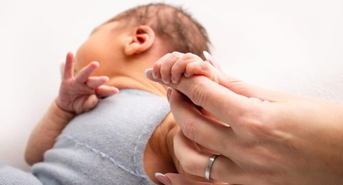 Close-up little hand of child and palm of mother and father. The newborn baby has a firm grip on the parent's finger after birth. A newborn holds on to mom's, dad's finger.